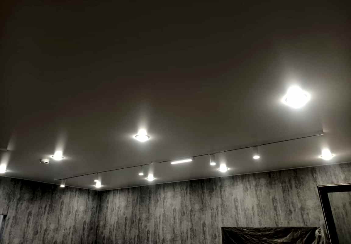 Треки и точечные светильники в матовом натяжном потолке в гостиной.