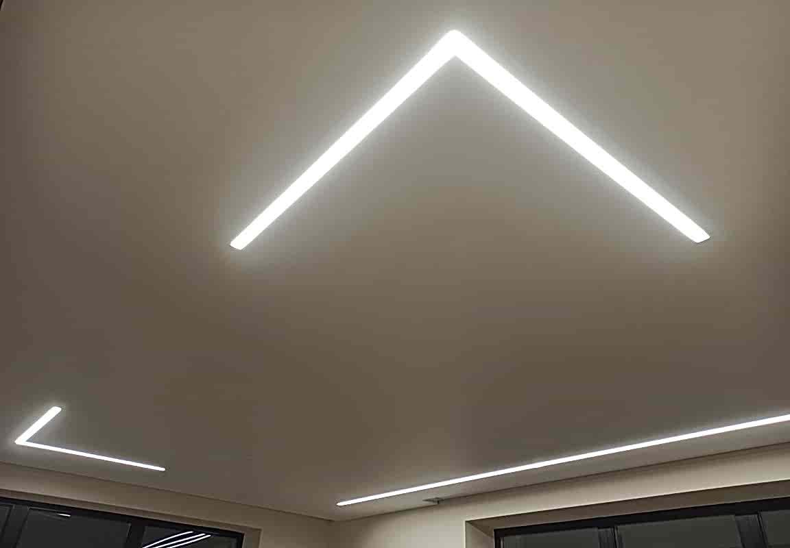 Геометричная подсветка углов в гостиной и матовый натяжной потолок.