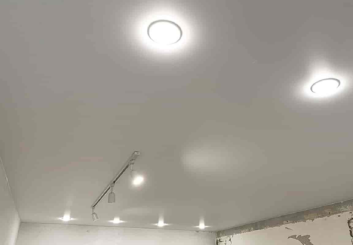 Накладной трек и белые светильники GX 53 в матовом наятжном потолке.