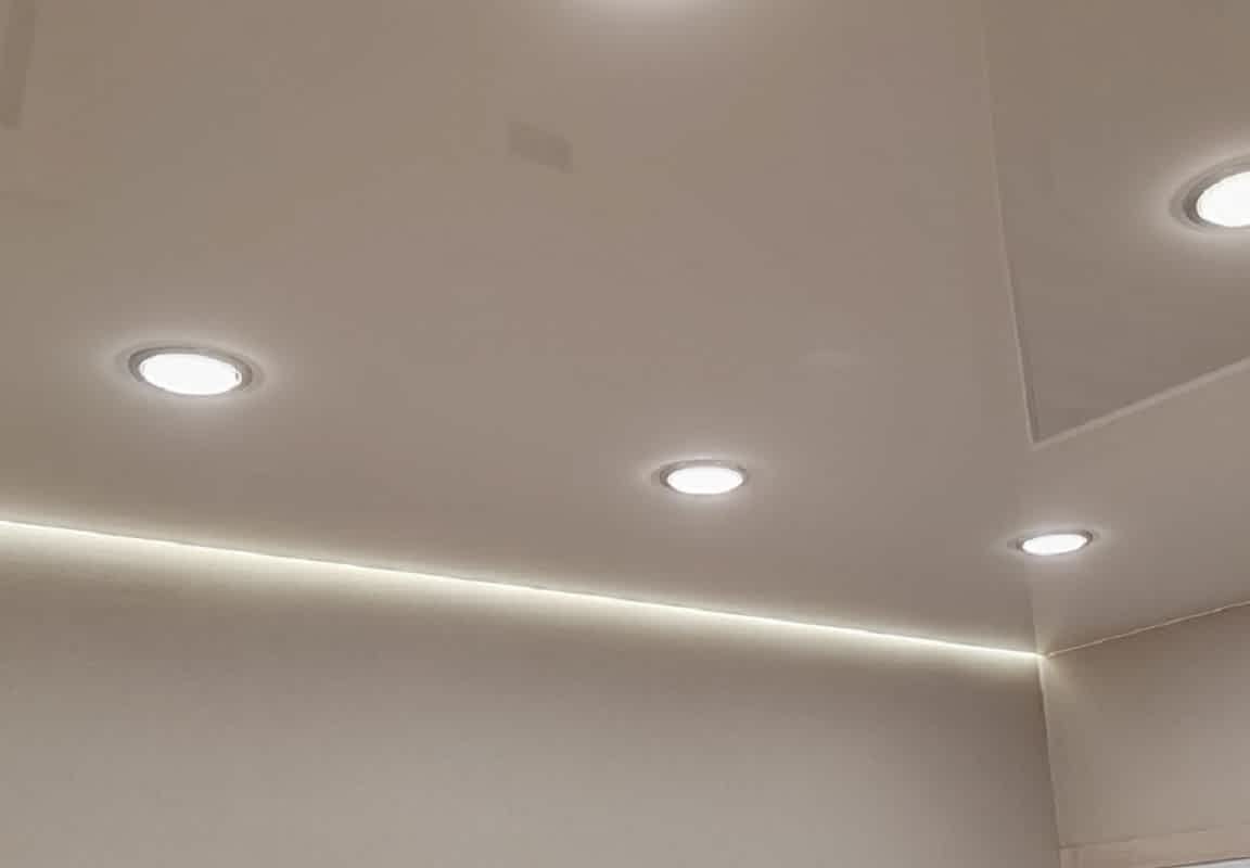 Бежевый глянцевый натяжной потолок и точечные светильники.