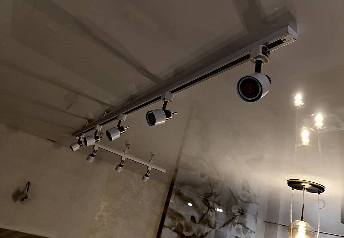 Глянцевый натяжной потолок в кухне-гостиной с накладным трековым светильником.