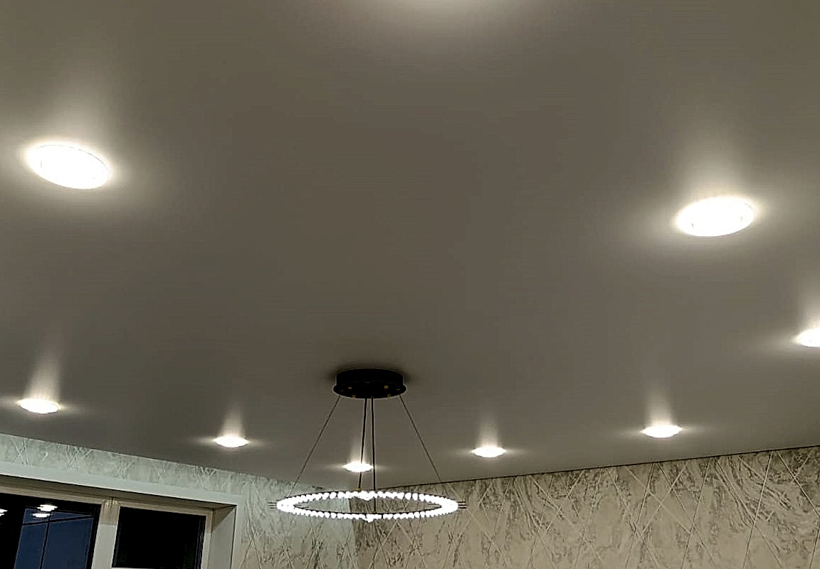 Интерьер гостиной с 10 точечными светильниками,люстрой и нишей под гардину в сатиновом натяжном потолке.