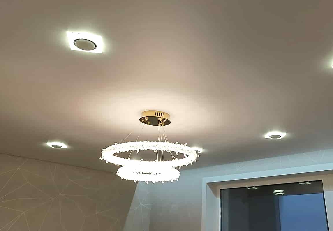 Сатиновый натяжной потолок в интерьере гостиной и квадратные точечные светильники.